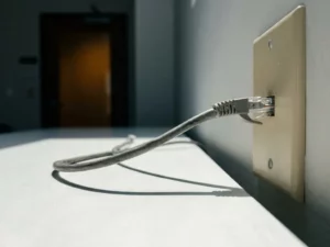 Ethernet-Kabel in ungesicherter Büro-Wandsteckdose mit dramatischem Schatten auf weißem Schreibtisch, Makroaufnahme.